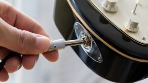 エレキギターのジャックにシールドケーブルのプラグを挿している手元