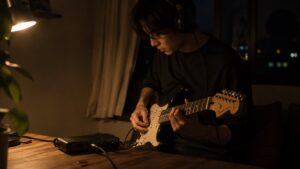 夜の部屋でヘッドホンをつけてエレキギターを弾く人物とオーディオインターフェース